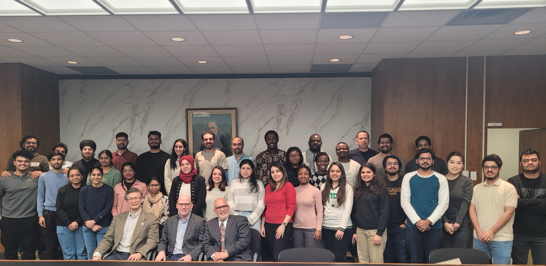 A diverse group stands in a well-lit conference room, with three seated in the front row, posing with a guest speaker.